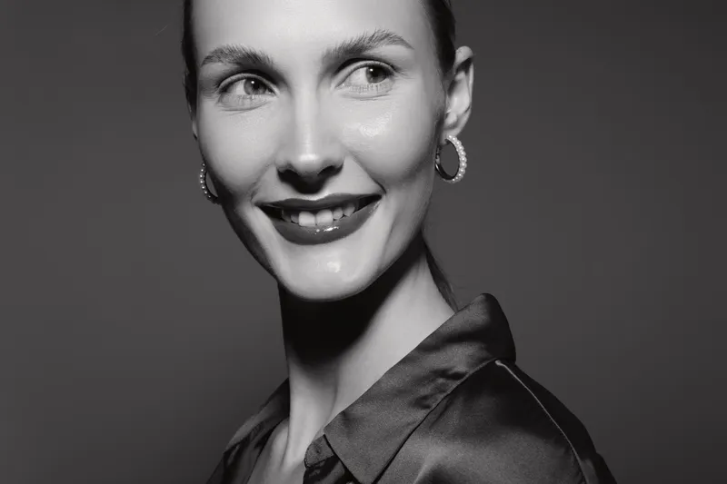 Portrait of a smiling white woman with light skin wearing hoop earrings and a satin blouse. Studio shot in black and white with soft lighting and natural makeup. Concept of happiness.