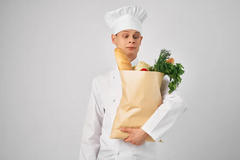 Весёлый мужчина-шеф-повар с пакетом продуктов работает на кухне