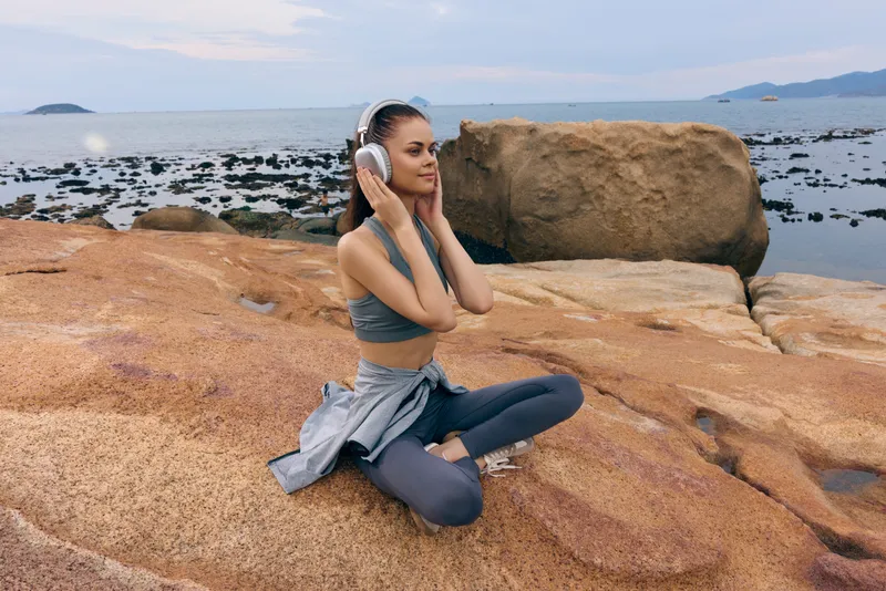 Young woman enjoying music with headphones on a rocky beach, reflecting happiness and tranquility in a serene coastal environment