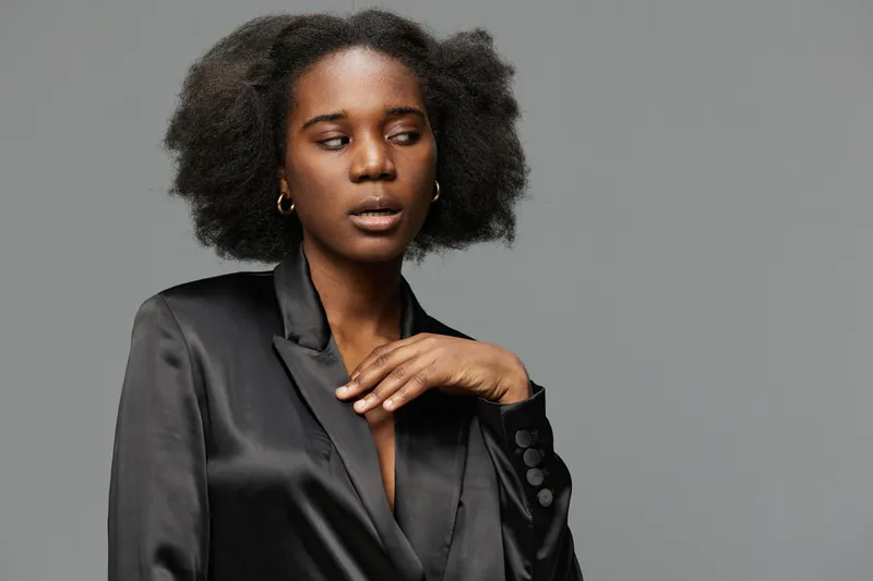 Stylish African model in a black satin blazer with textured hair, conveying a confident and sophisticated look against a gray background