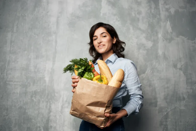 Женщина с пакетом продуктов покупает овощи