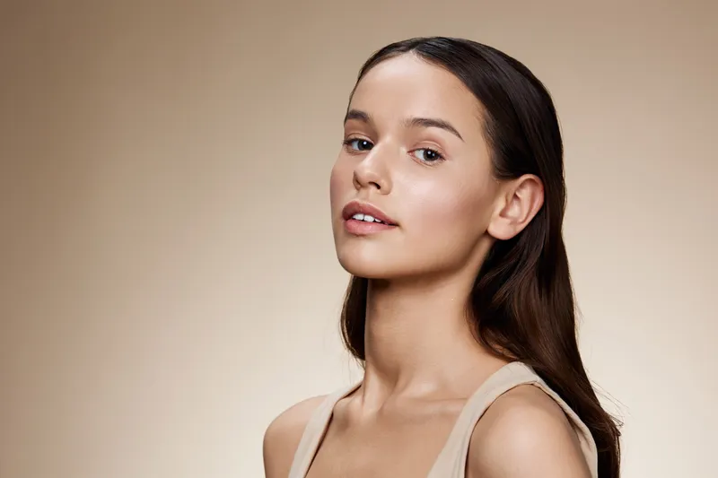 Beautiful young woman with natural makeup and long hair on a neutral background, embodying confidence and elegance in a minimalistic lifestyle concept
