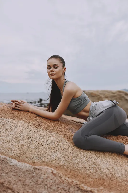 Young woman in activewear poses on a rock, showcasing a healthy lifestyle and fitness Calm emotions, nature backdrop, ideal for wellness themes