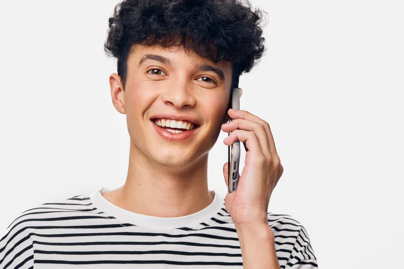 smiling man talking on smartphone wearing striped shirt with curly hair isolated on white background expressing happiness and communication