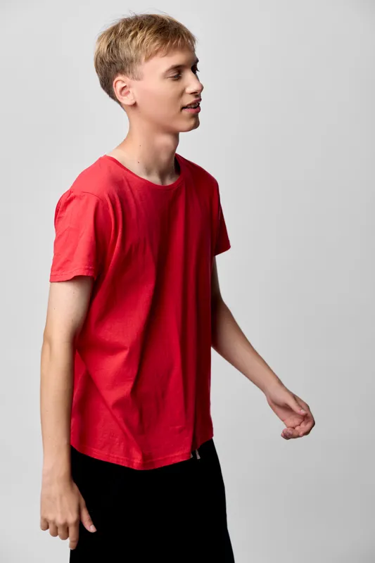 Boy in a red shirt, side profile, standing against a neutral background in a simple studio setting, casual wear focus, clean lines and relaxed posture for fashion and lifestyle use