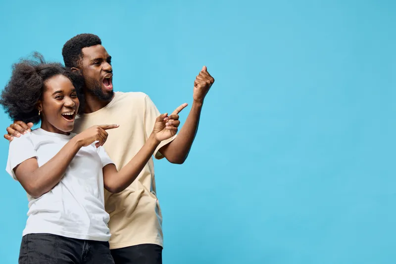 Happy couple celebrating with excitement, showcasing emotions in casual attire against a vibrant blue background, perfect for joyful themes or promotions