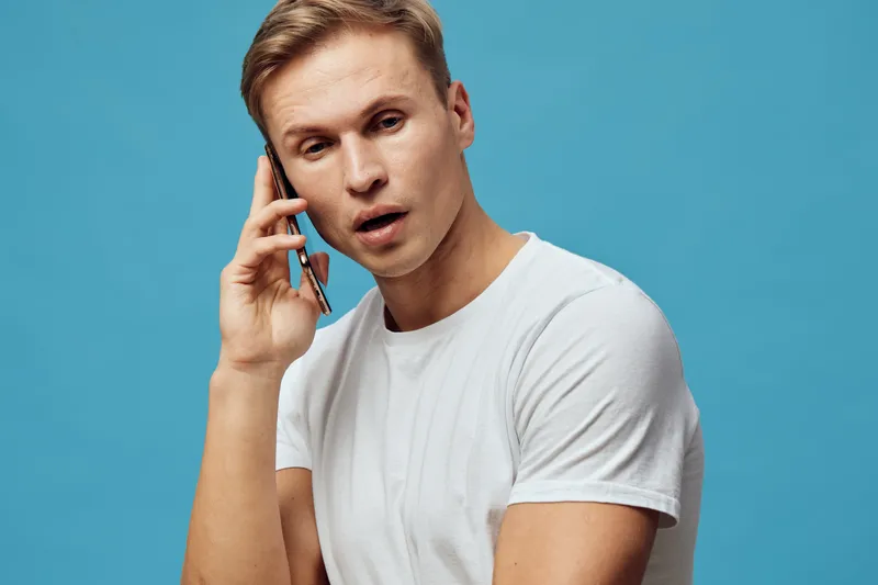 Young caucasian man talking phone white t-shirt blue background smartphone communication digital nomad concept