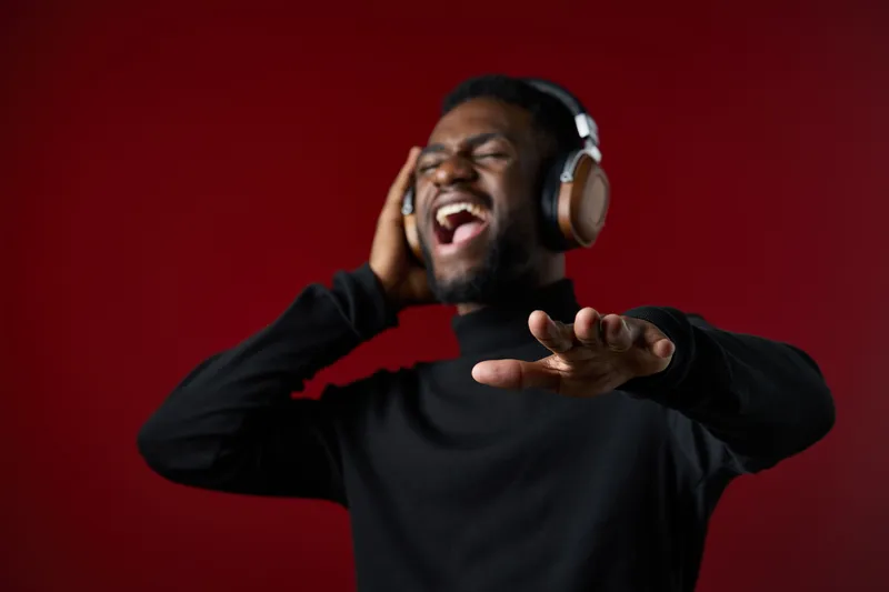 Young Black man enjoying music with headphones, singing passionately in a studio against a deep red background