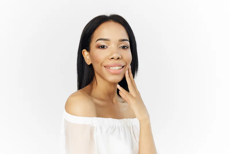 Женщина африканской внешности в белом платье позирует с косметикой, роскошь, светлый фон