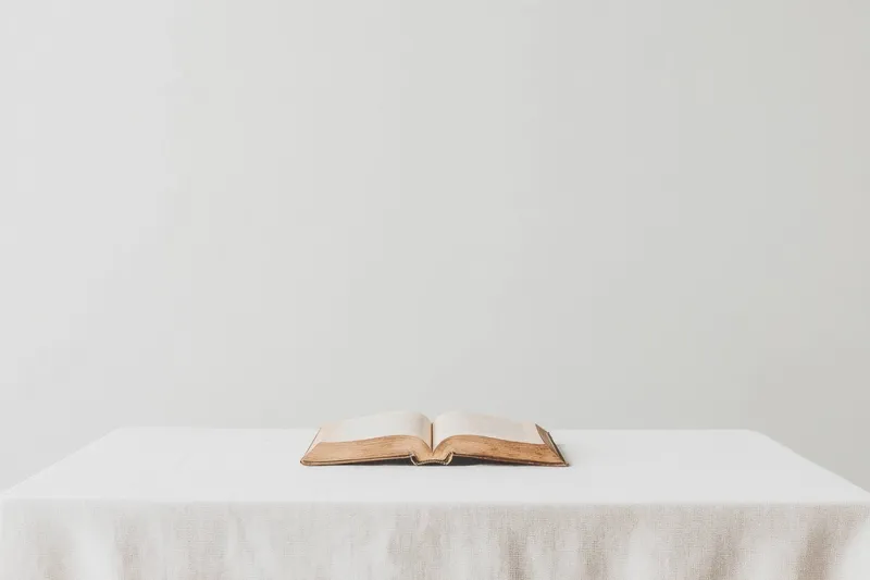 Открытая книга лежит на белом столе на минималистичном фоне, олицетворяя знания, образование, мудрость и вдохновение