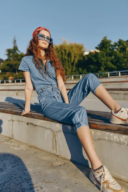Lifestyle woman in modern boho-western denim street style poses confidently outdoors with a relaxed attitude and film color creating a vintage, sunlit mood.