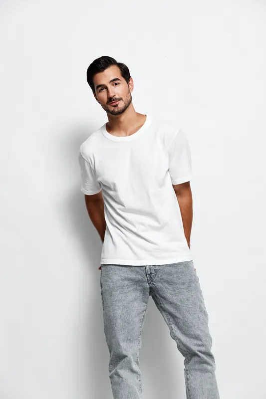 Stylish young man in a white t-shirt poses confidently with a charming smile, isolated on plain background. Fashion and lifestyle concept.
