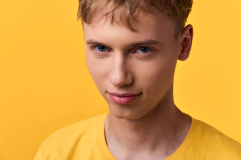 Closeup of a smiling young man in a casual yellow shirt against a bright yellow backdrop, capturing youth energy, simple fashion style, and bold color harmony for lifestyle or beauty themes