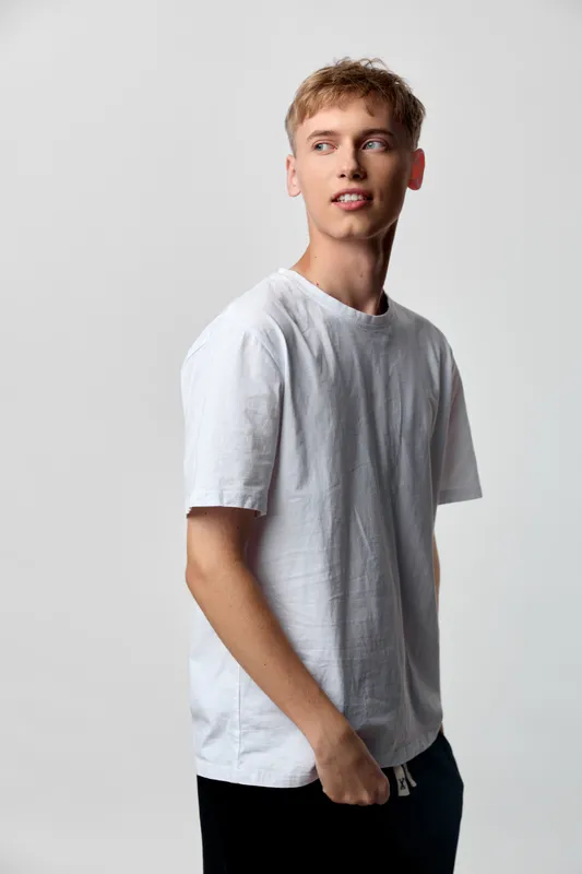 Man wearing a plain white tee stands against a neutral backdrop, relaxed pose, casual fashion, everyday style, minimal wardrobe, clean lines, lifestyle image for stock use, versatile and timeless