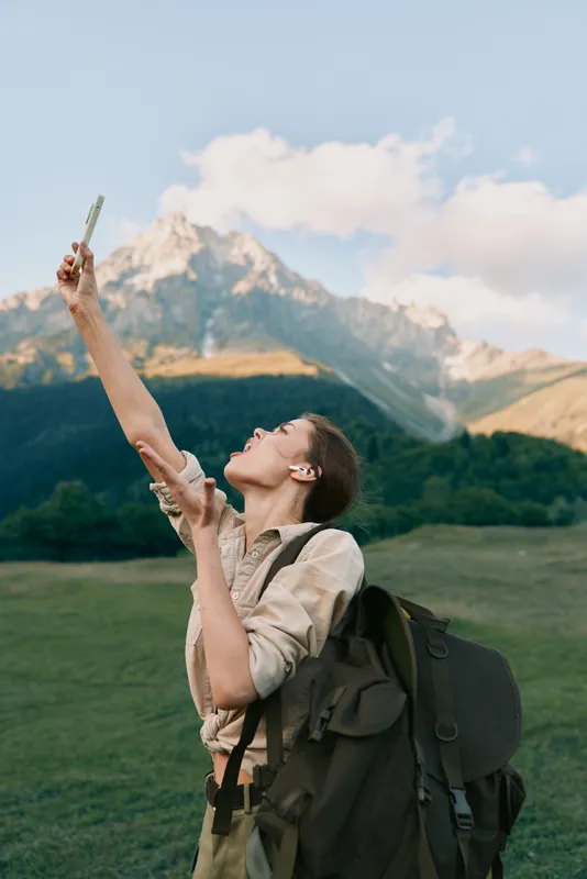 Smiling woman with backpack raises a map toward the sky in a green meadow with mountains in the background, showing outdoor exploration and personal travel in a vivid natural setting