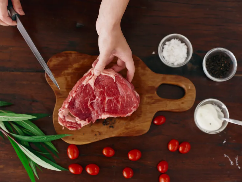 Женщина с ножом в руке нарезает свежее стейковое мясо для жарки на кухне