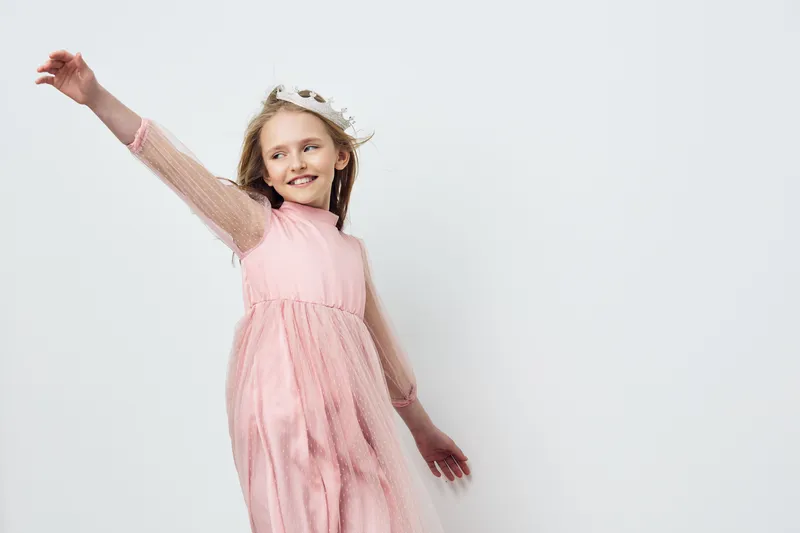 Joyful young girl in a pink dress dances against a minimalistic background, expressing happiness and freedom with her arms outstretched