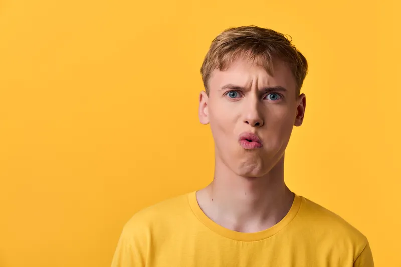 Male figure in a yellow shirt against a bright yellow background making a puckered lips expression, studio style with bold color, playful mood, expressive emotion for stock use