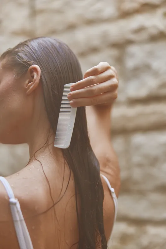 woman combing wet hair with white comb, close-up, natural light, soft focus, healthy hair care, serene moment