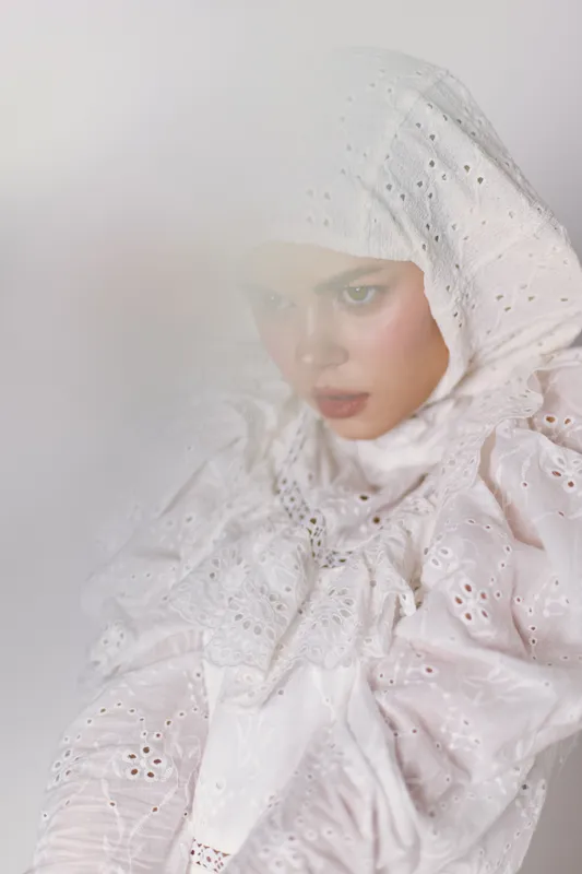 Elegant young model in a white lace hijab, showcasing serene emotions against a soft, blurred background, embodying purity and cultural beauty