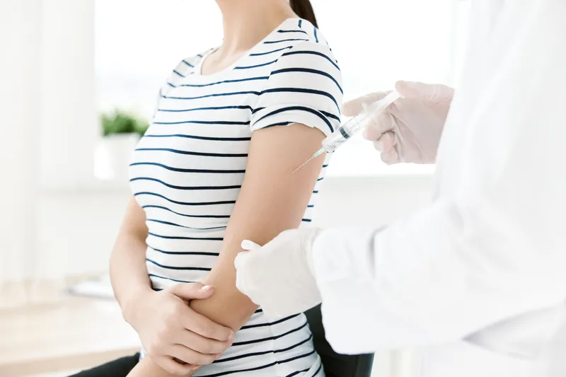 Врач в белом халате делает инъекцию вакцины в руку пациента