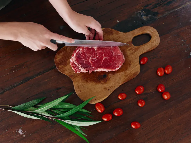 Женщина с ножом в руке нарезает свежее мясо стейка для жарки на кухне