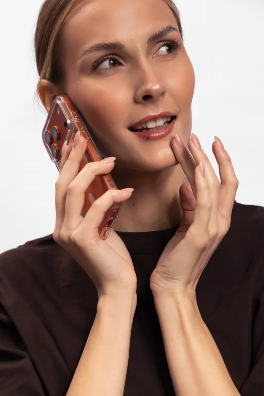 Young woman with clear skin holds smartphone near ear and smiles thoughtfully. Close-up portrait on white background. Concept of communication, technology, and modern lifestyle.