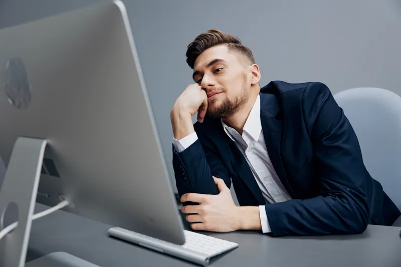 Уставший менеджер с чашкой кофе работает за компьютером