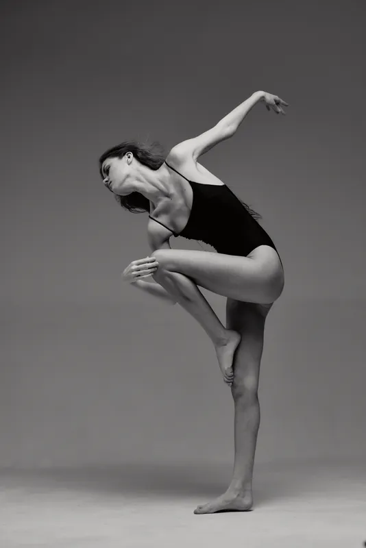 graceful woman dancer posing in black leotard with elegant posture in black and white minimalistic studio