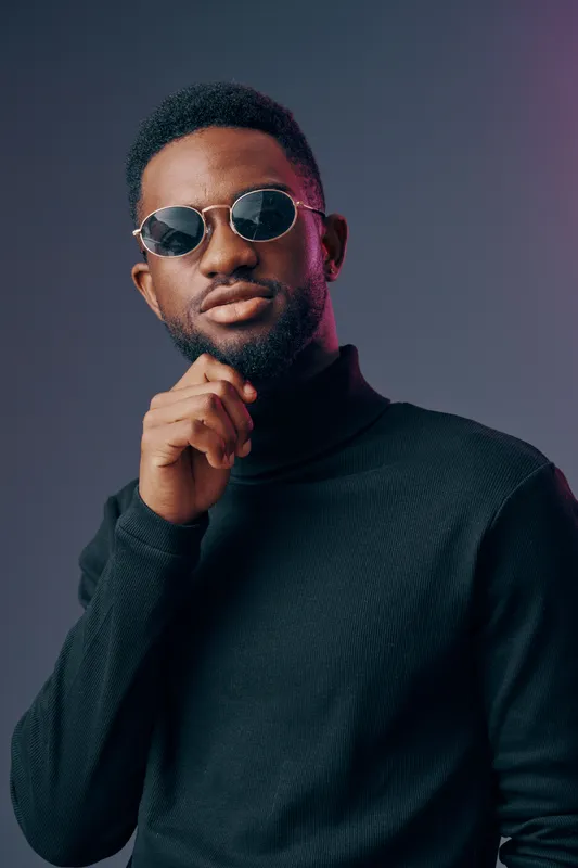 Stylish young man in black turtleneck and sunglasses posing confidently against a two tone background with a modern vibe