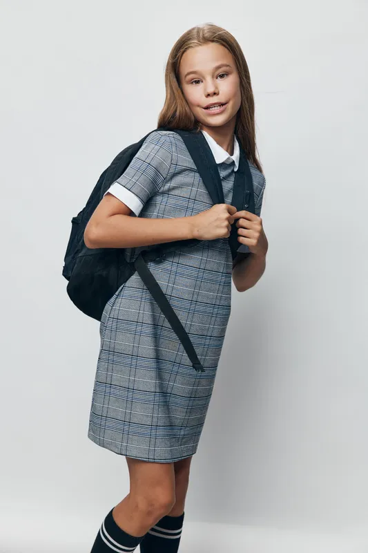 Girl student with backpack in school uniform standing and smiling on light background. Child, education and schoolgirl in casual style with long hair preparing for study day.