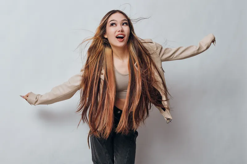 Young woman with long braided hair posing in casual clothing with arms outstretched on light background for fashion and beauty portrait.