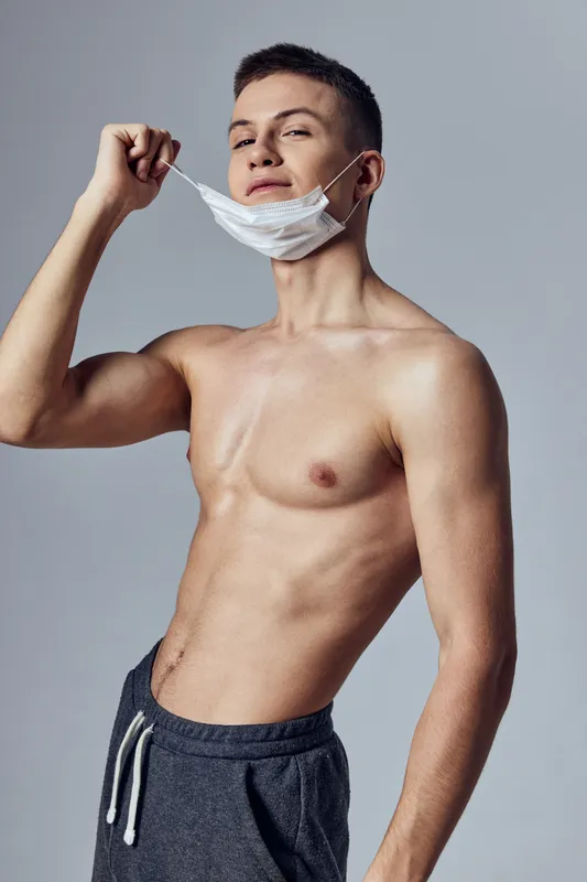 Спортивный мужчина в медицинской маске с надутым торсом, защита здоровья на изолированном фоне