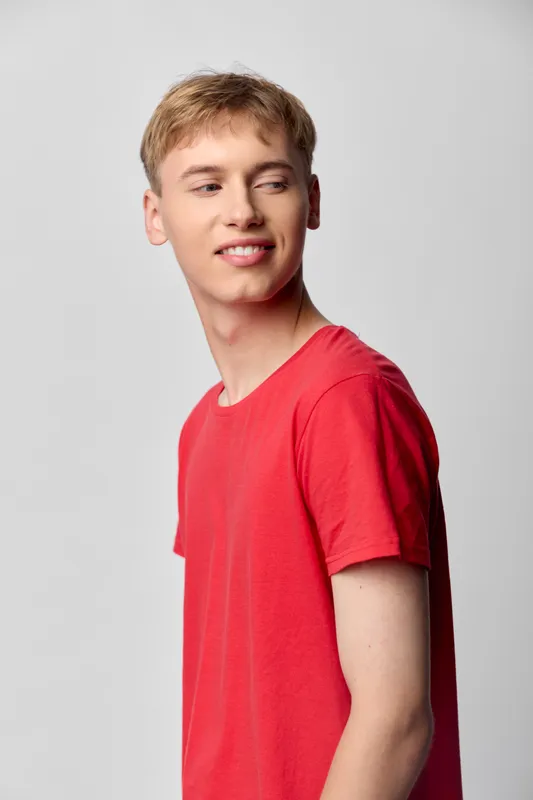 Smiling young man in red t shirt, casual lifestyle, fashion, confidence shot in a neutral studio, ideal for youth, everyday style and approachable vibes