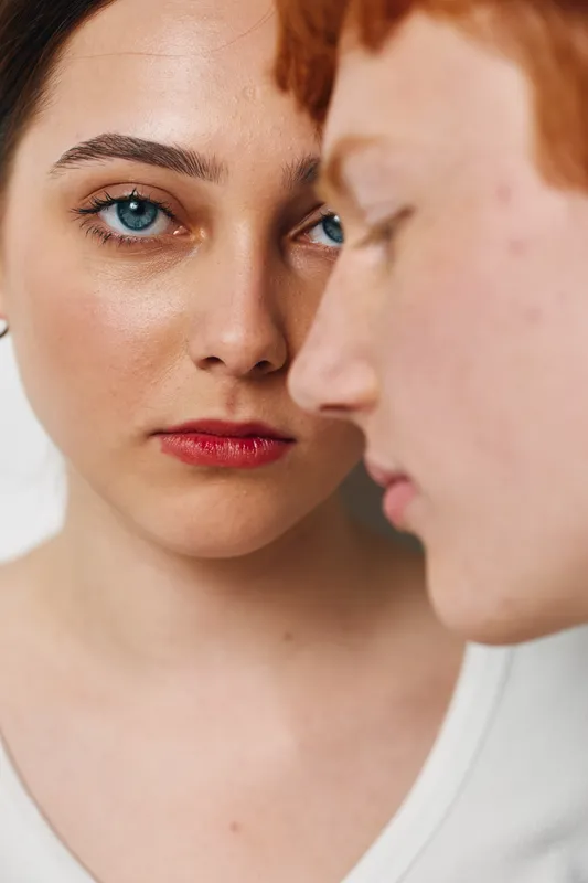 Portrait of woman with blue eyes looking at camera close to man with red hair, both with natural skin and neutral expression on white background in studio shot.