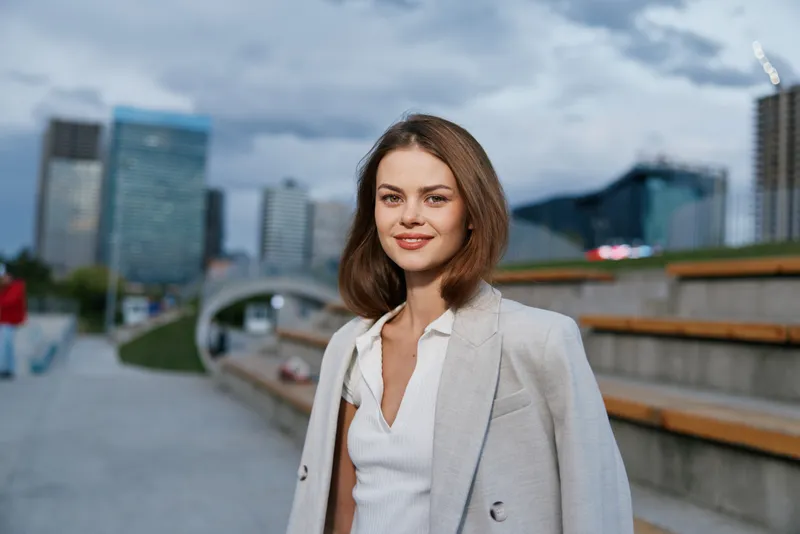 confident woman in business attire outdoors in urban environment with modern buildings and cloudy sky, casual style, professional appearance