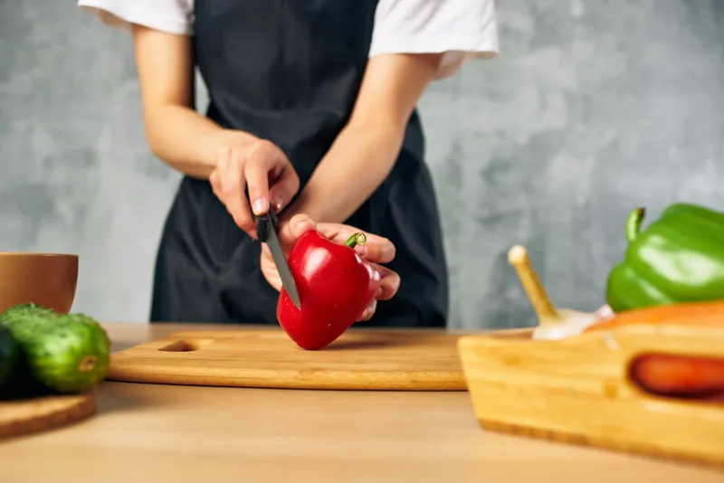 Женщина в черном фартуке на кухне нарезает овощи