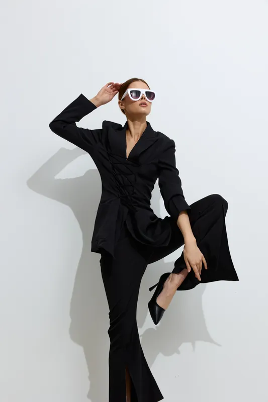 fashion woman in black suit poses confidently with white sunglasses, stylish and modern, minimalistic background, professional look with sharp lines.