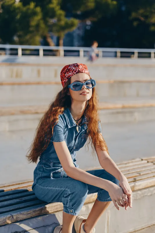 Lifestyle woman in modern boho-western denim street style wearing sunglasses and a red bandana, relaxed outdoor portrait with film color effect and sunny atmosphere.