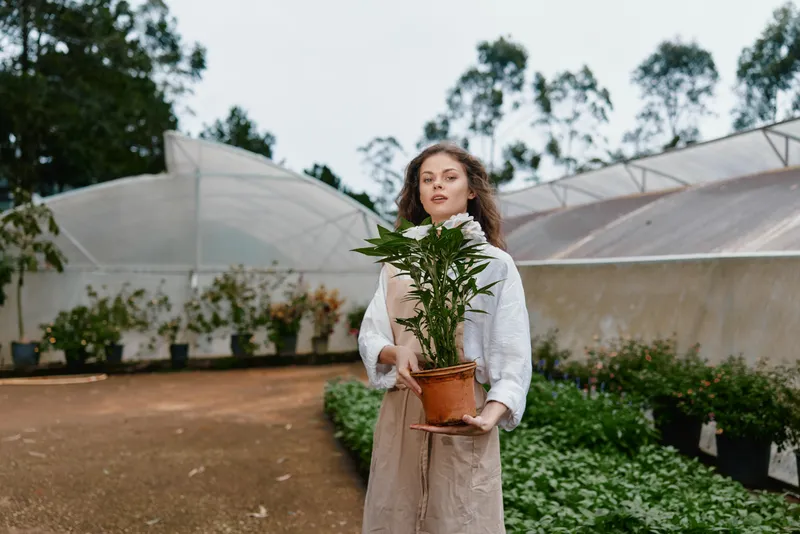 Young woman holding a potted plant in a greenhouse, showcasing a connection with nature, dressed casually in earthy tones, expressing joy and serenity