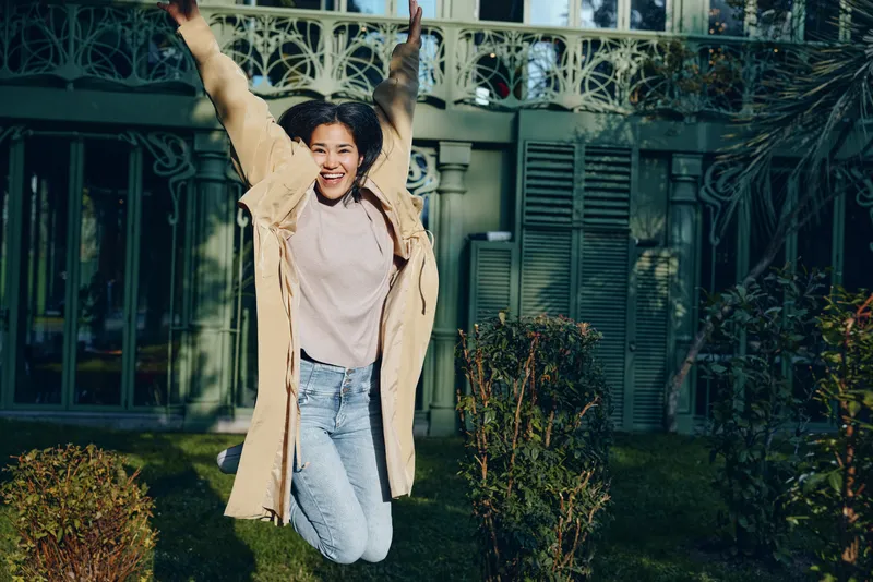 Joyful jump in a cozy coat outdoors, a candid moment of energy and laughter in a garden setting, casual fashion, motion and happiness captured during a spontaneous celebration