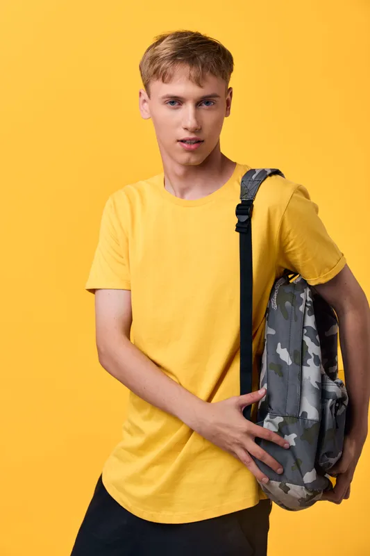 Youth wearing a yellow tee carries a camo backpack against a bright yellow backdrop, showcasing casual style, modern schoolwear, and readiness for daily adventures.