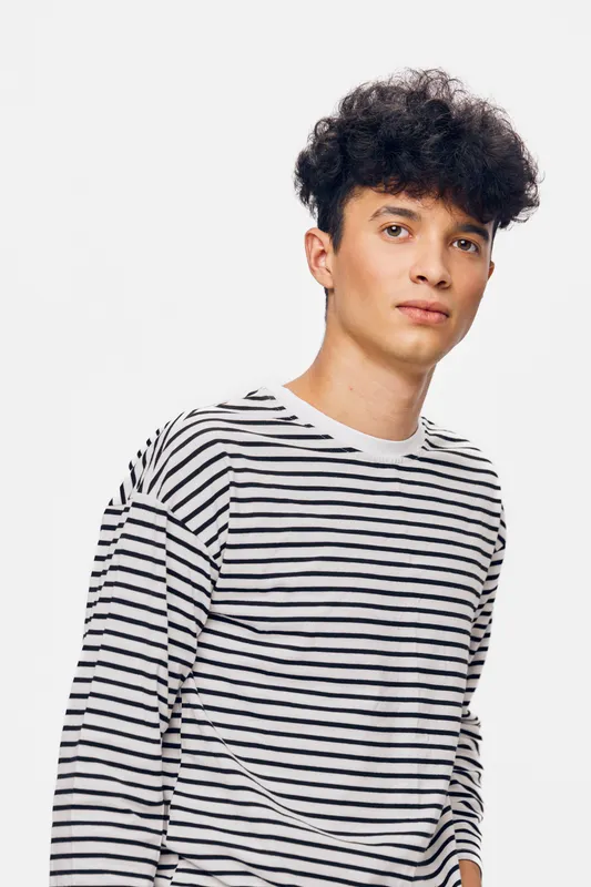 young man wearing striped shirt with casual hairstyle against plain white background, looking confident and relaxed for portrait