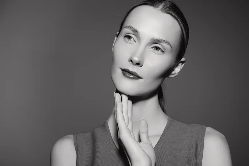 Portrait of a young white woman with fair skin and slicked hair posing with hand near face, looking thoughtful in monochrome studio.