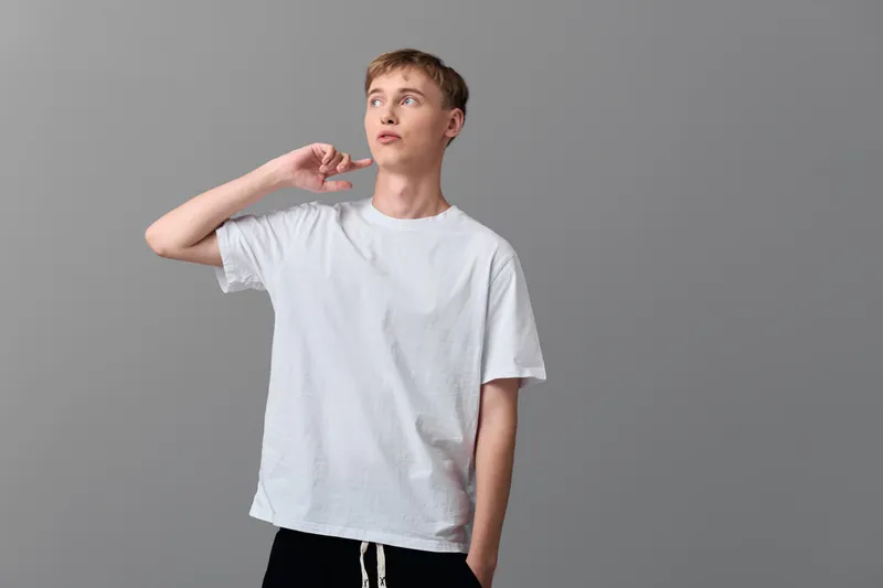 Man listening in a studio, casual vibe, wearing a white t shirt, relaxed pose against a neutral gray background, showcasing simple fashion and focused mood