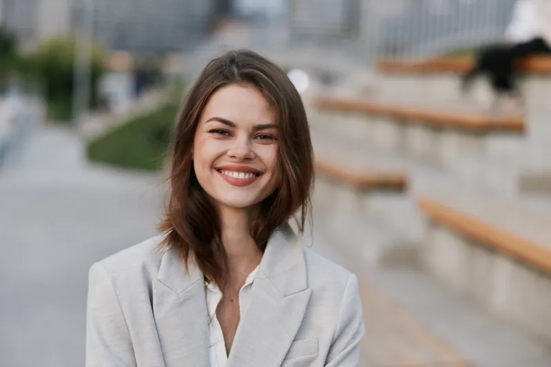 confident woman smiling in light gray blazer outdoors urban background business portrait autumn season