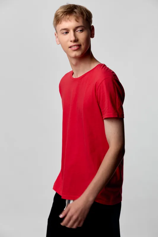 Red t shirt worn by a young man in casual studio setting, relaxed standing pose, simple background, fashion inspired, everyday wardrobe, clean lines and minimal styling