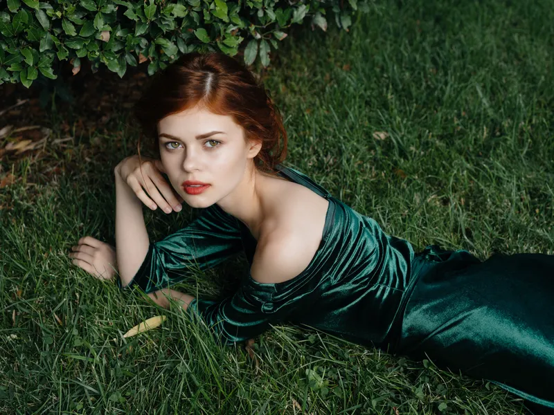 Красивая женщина в зеленом платье лежит на траве в сказочном саду