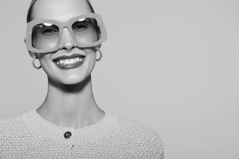 Smiling white woman with light skin and large glasses wearing a knitted sweater in studio. Close-up portrait with positive mood, fashion style and eyewear concept.