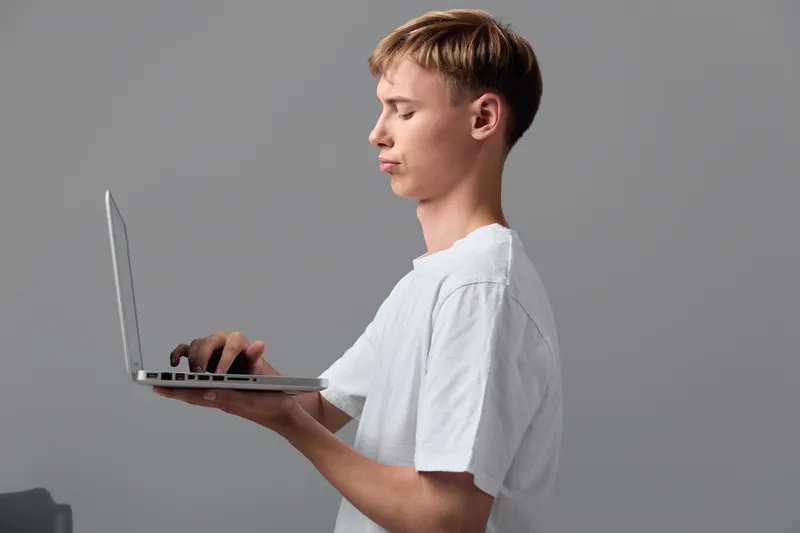 Man with a laptop in hand, side view profile, focused on screen for remote work, learning and digital tasks, showcasing device use and concentration in a modern setup